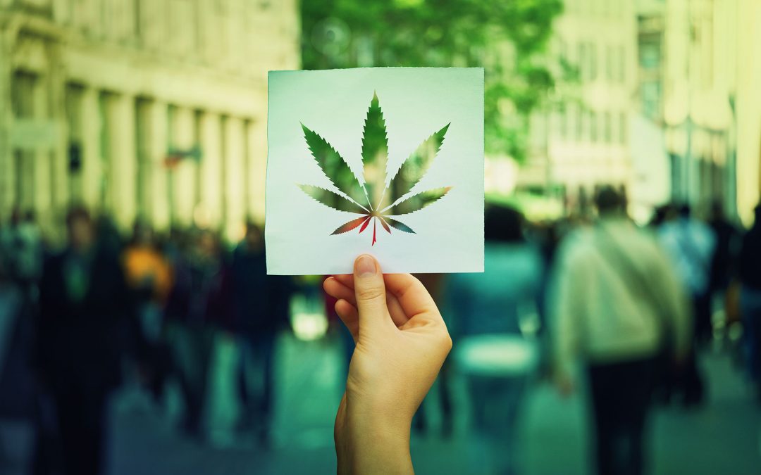 hand holding cannabis leaf cut out on busy street